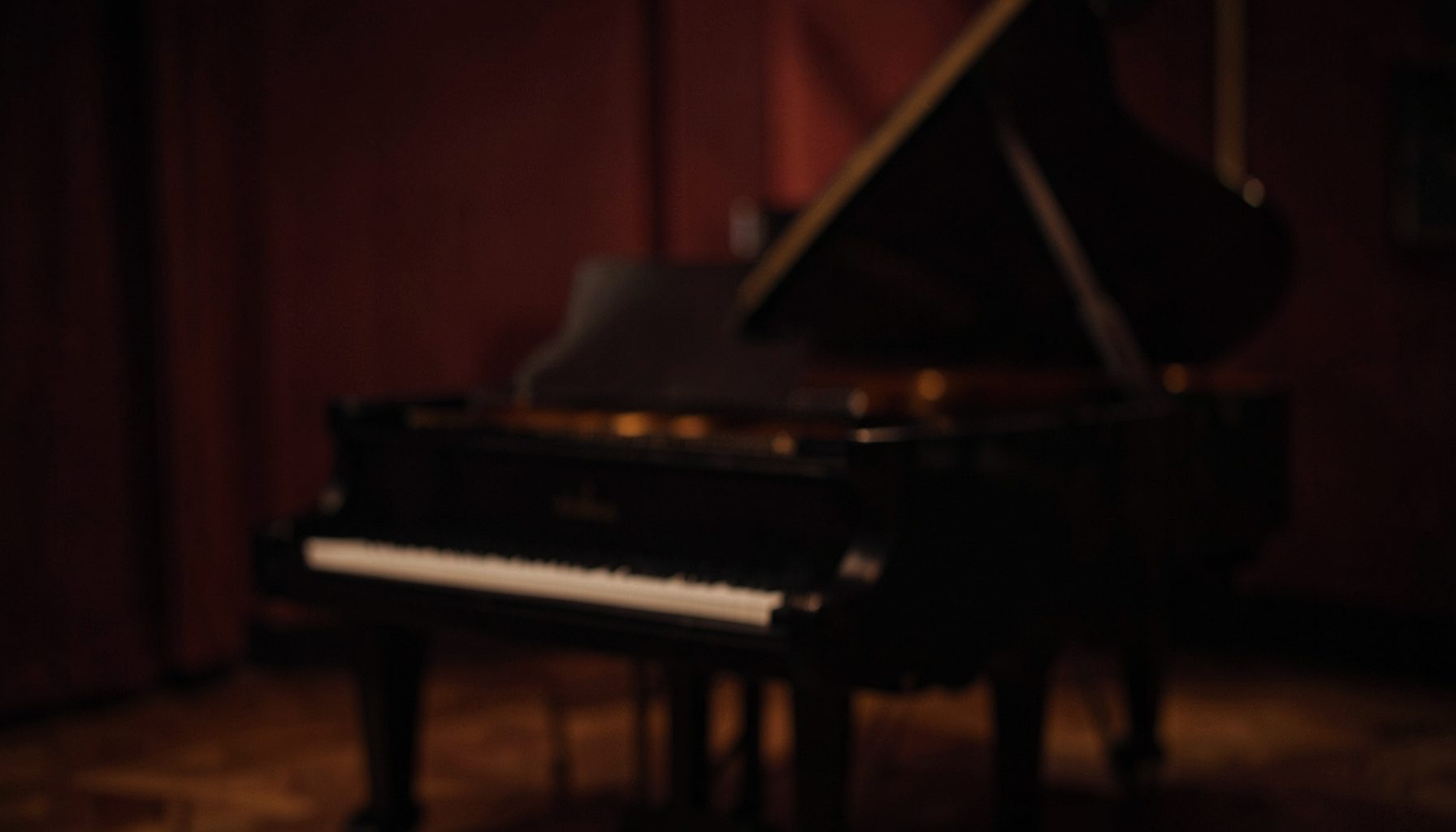 A warm, dimly lit studio interior with a grand piano in soft focus, deep burgundy and amber tones, moody and intimate atmosphere.